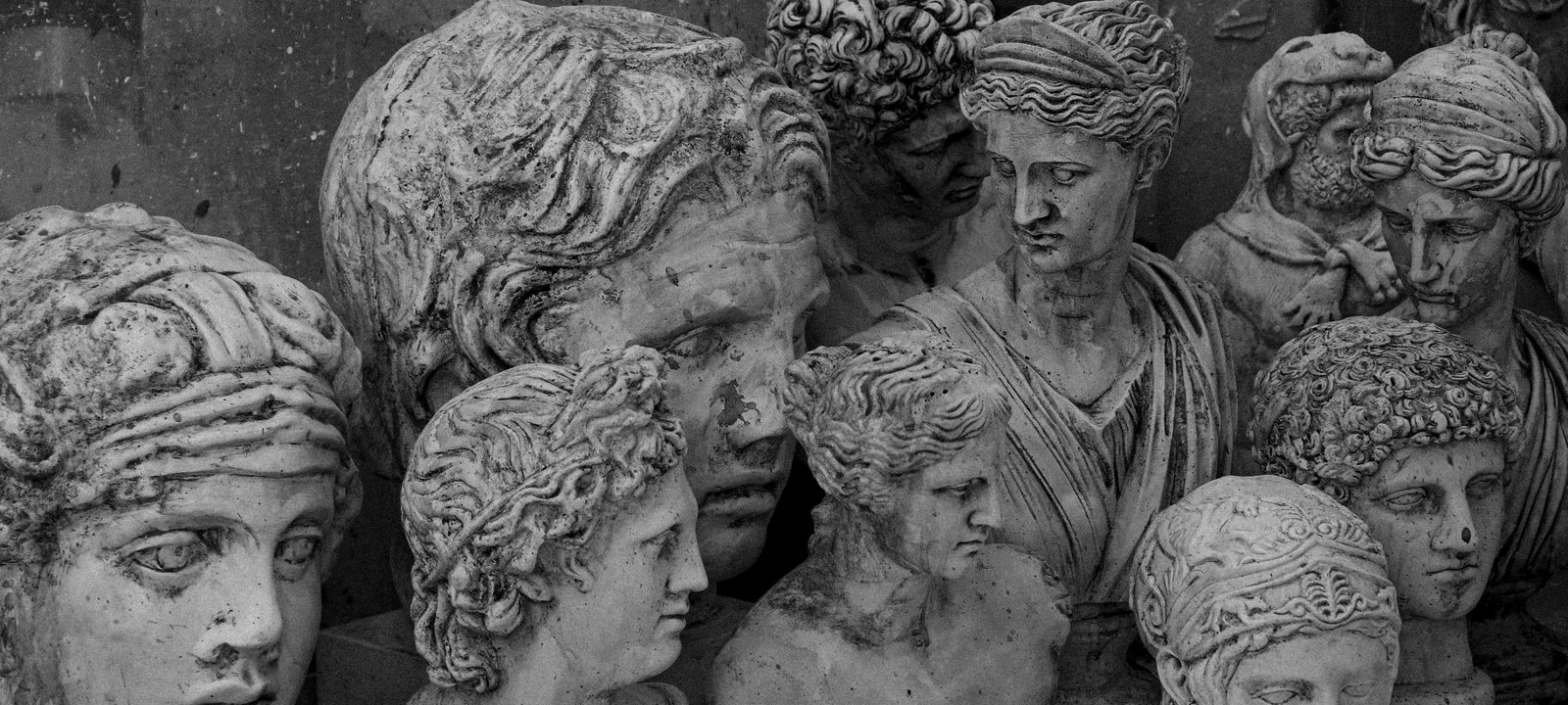 A group of vintage stone head bust sculptures in grayscale, depicting ancient figures.