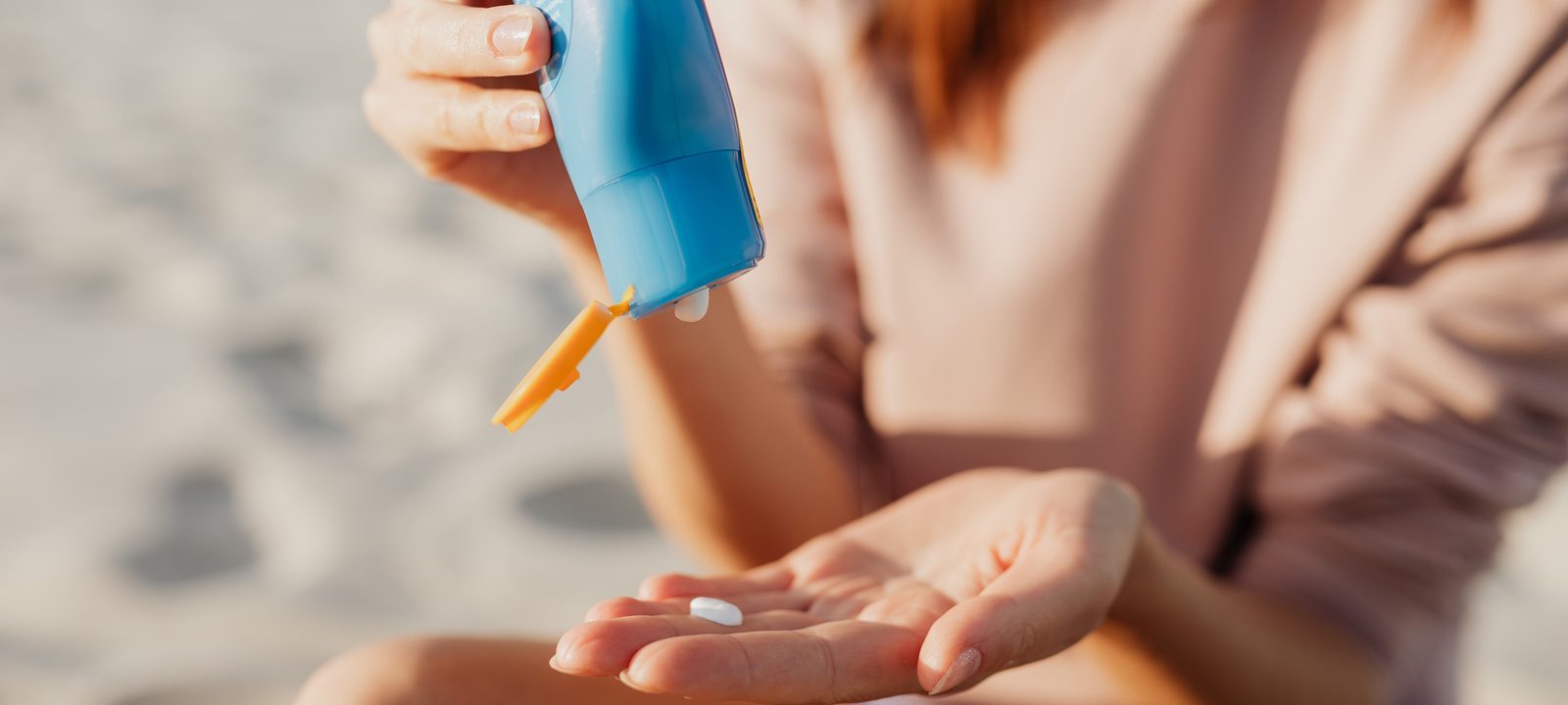 A person applies sunscreen at the beach on a sunny day.