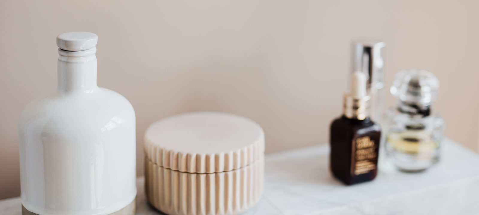 Set of reusable cosmetic containers for cream and shampoo arranged near various skincare products and perfume bottle on white marble shelf against beige wall in modern bathroom interior