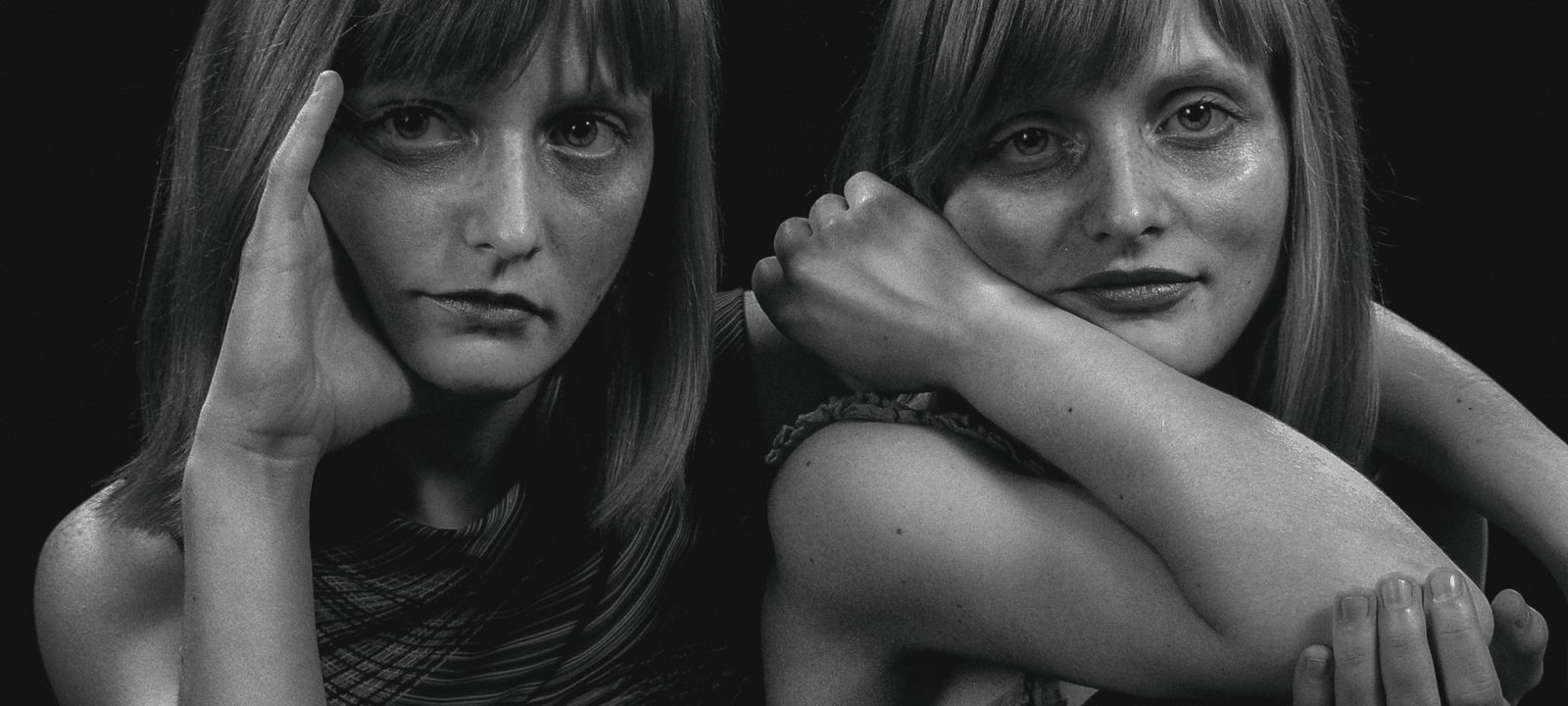 Artistic black and white portrait of twin women posing together in a studio setting.